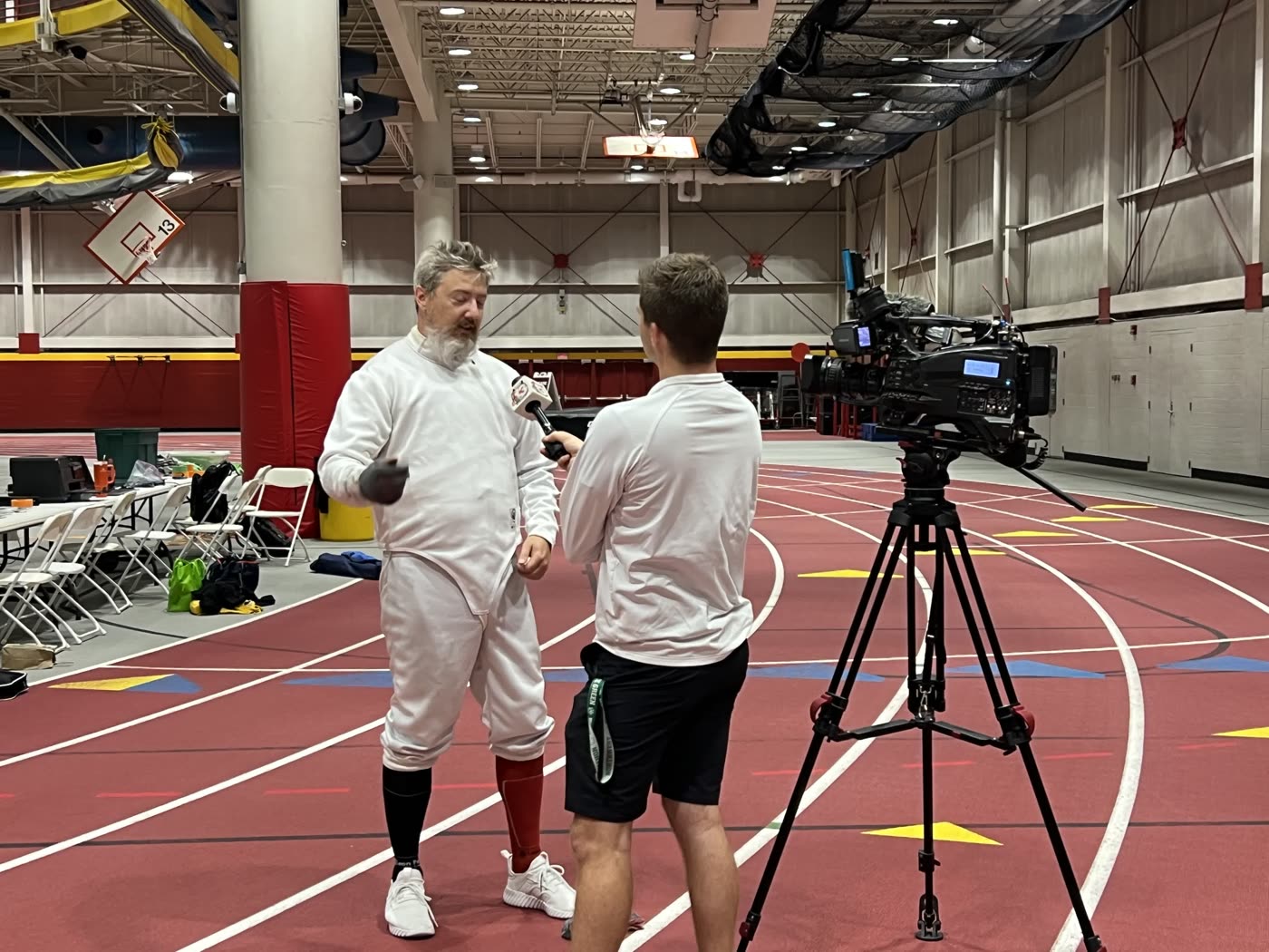 Eric Rhea in fencing whites being interviewed on camera by a WHO13 reporter at the Iowa Games